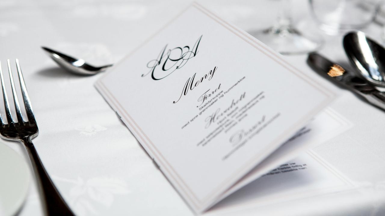 Elegantné svadobné menu na stole pripravenom na špeciálnu udalosť s bielym obrusom a príborom.