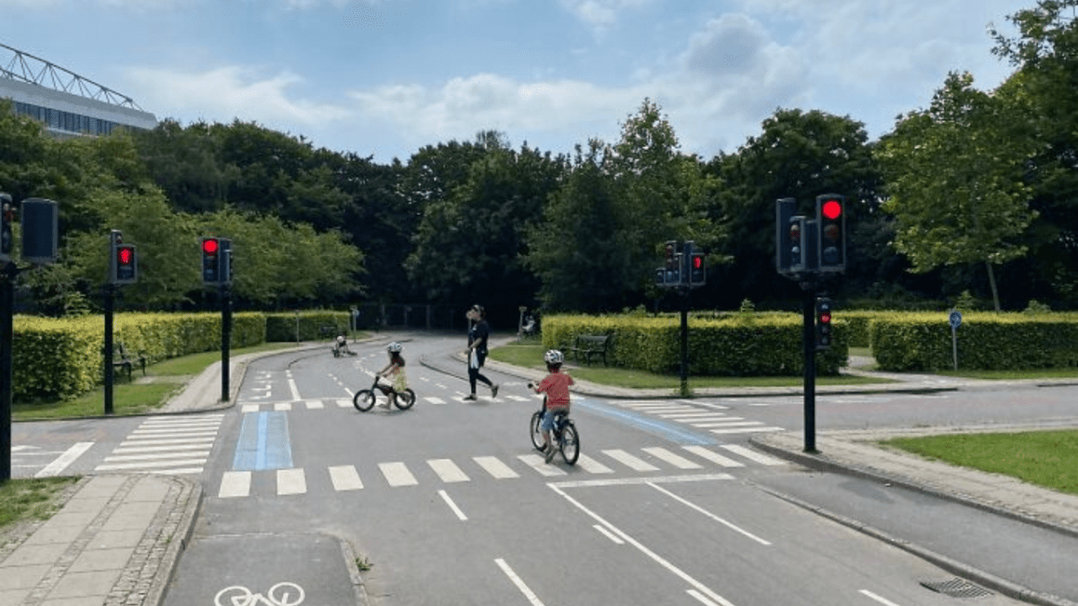 Deti na bicykloch na detskom dopravnom ihrisku s funkčnými semaformi a zebrami v parku.