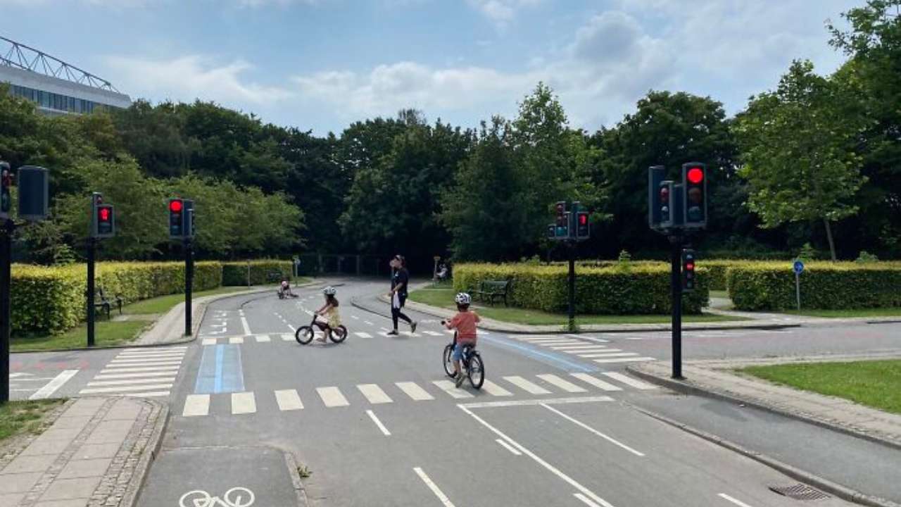 Deti na bicykloch na detskom dopravnom ihrisku s funkčnými semaformi a zebrami v parku.