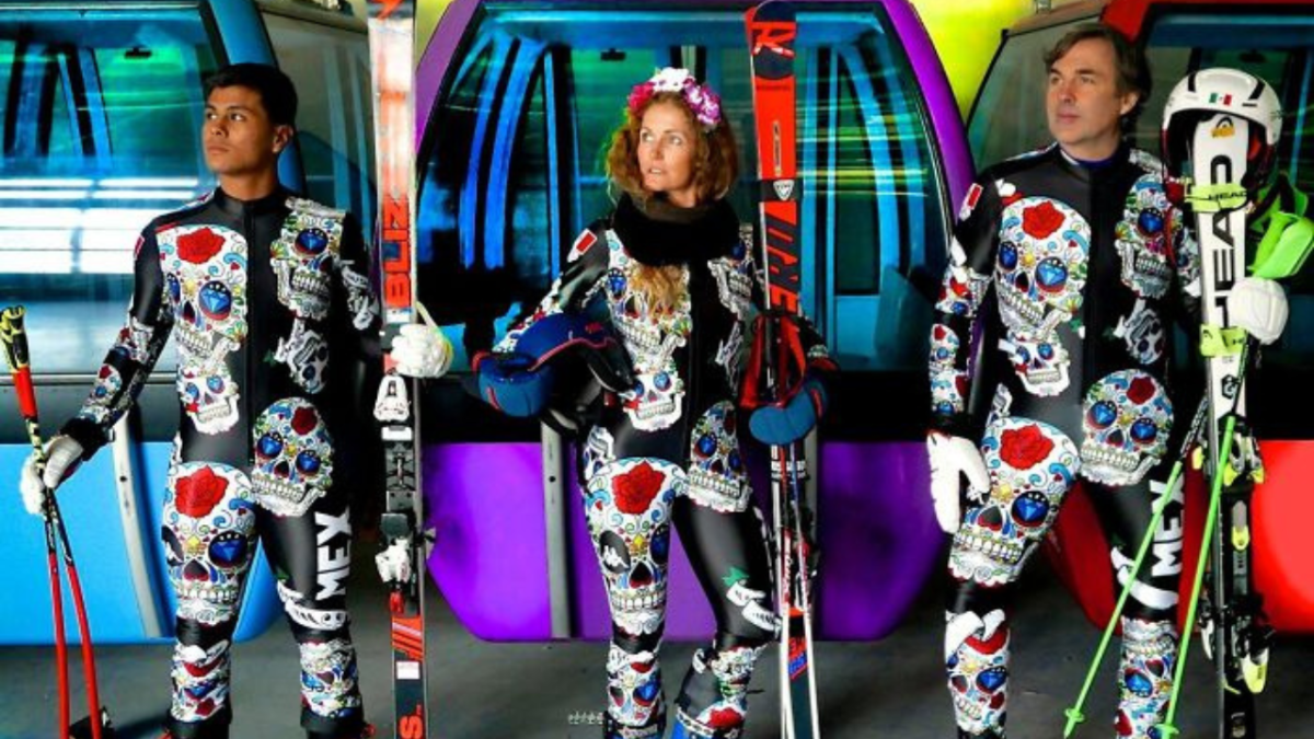 Lyžiari v jedinečných kostýmoch s lebkami, pripravení na svah pred pestrým pozadím lanovky.