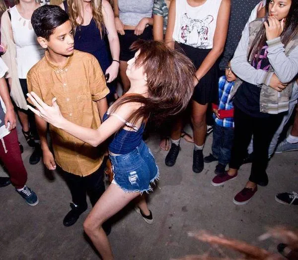 Skupina mladých ľudí na tanečnej párty, dievča energicky tancuje, okolo stojí divákov.