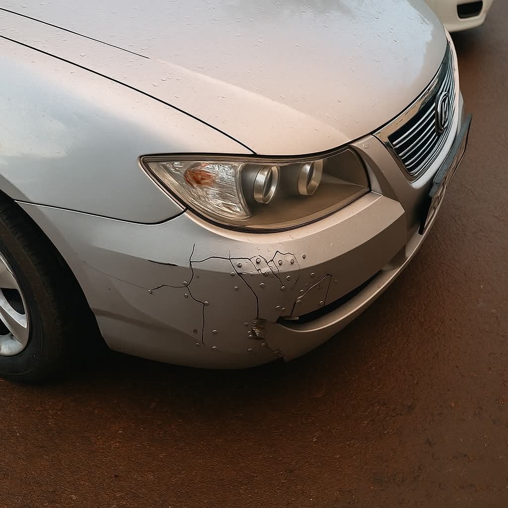 Strieborné auto s poškodeným predným nárazníkom a prasklinami na pravom rohu.