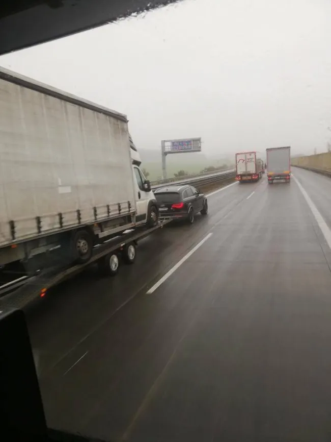 Auto ťahá príves s dodávkou na diaľnici za daždivého počasia.