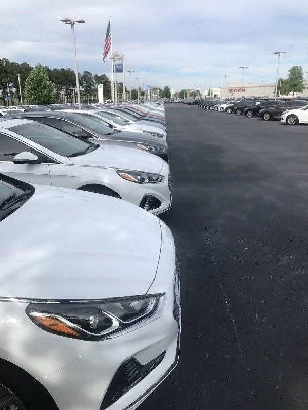 Rada moderných bielych áut na predaj v autosalóne s americkou vlajkou v pozadí.