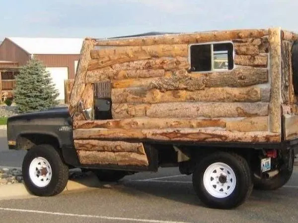 Auto s karosériou z drevených klád, zaparkované pri vidieckej budove, kreatívny dizajn na ceste.