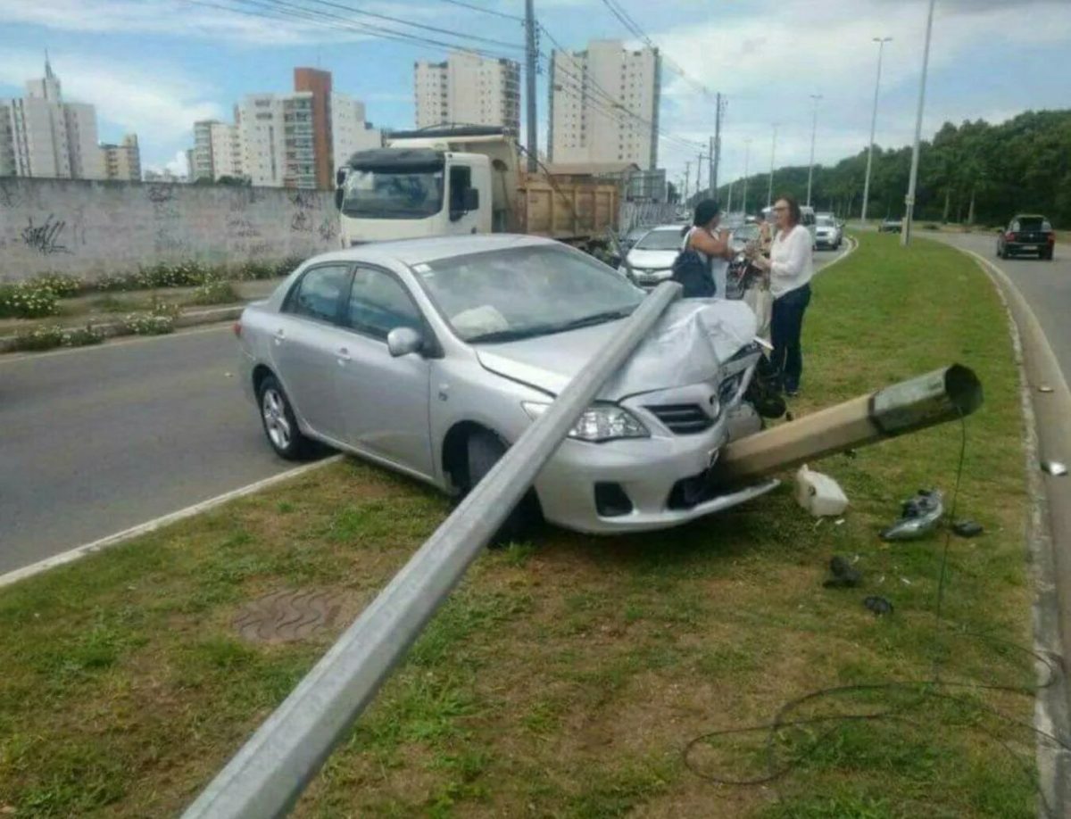 Auto nabúrané do stĺpu, dve osoby na trávniku komunikujú pri ceste, typická nehoda v mestskom prostredí.