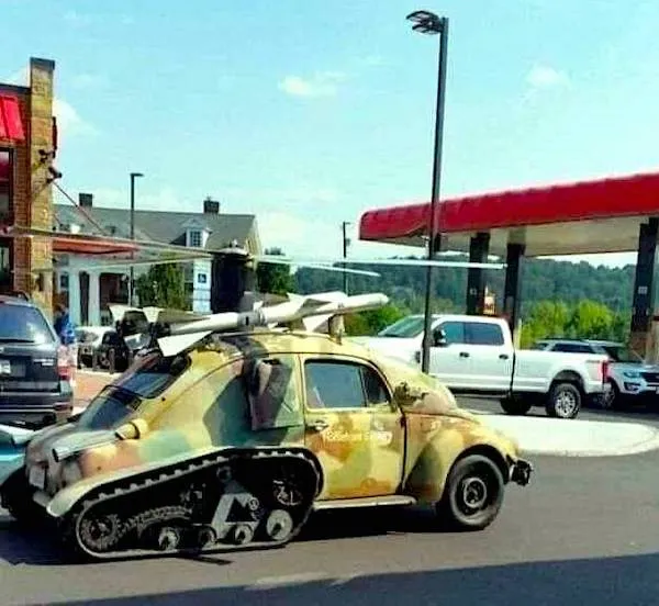 Staré auto s pásmi a raketami na čerpacej stanici, pripomínajúce vojenskú prestavbu.