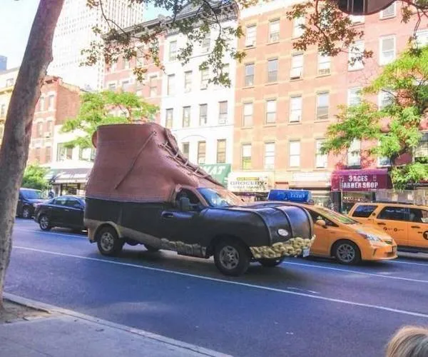 Auto v tvare obrovskej topánky prechádza rušnou mestskou ulicou.