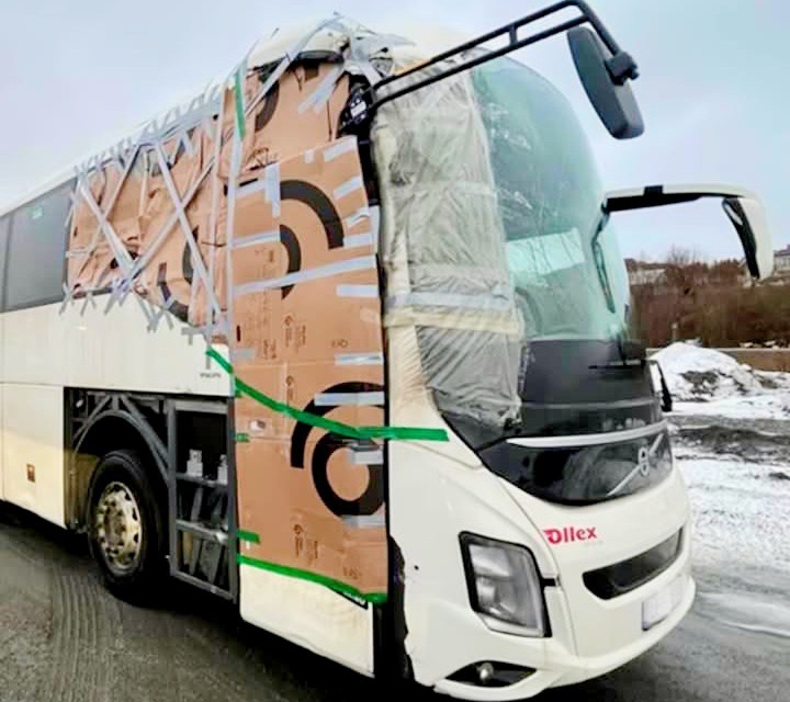 Autobus s provizórne opraveným predkom kartónom a páskou, zaparkovaný na zasneženej ceste.