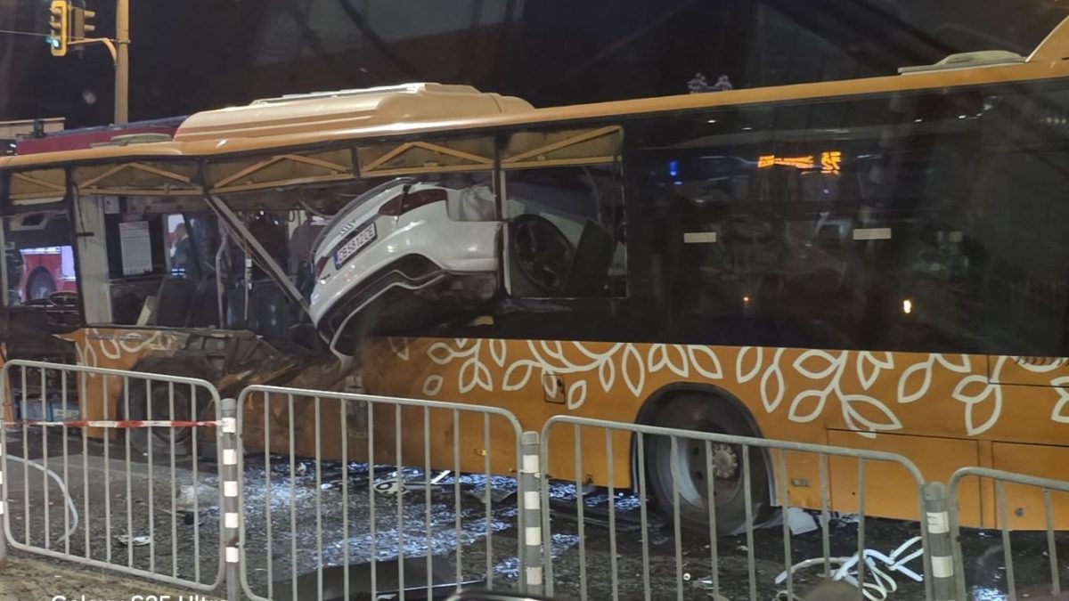 Auto zaseknuté v zadnej časti zničeného autobusu po nehode v noci, oplotenie okolo miesta nehody.