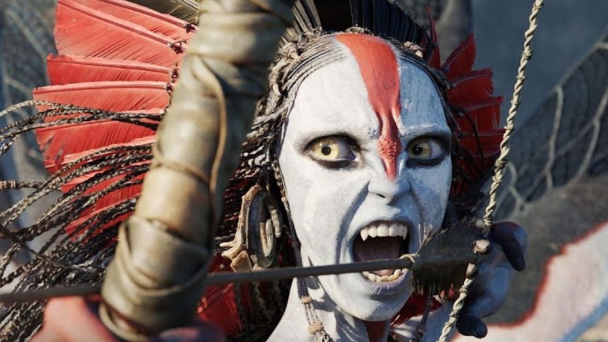 Kostýmovaný bojovník s intenzívnym výrazom a farebným perím v dramatickej póze počas napínania luku.