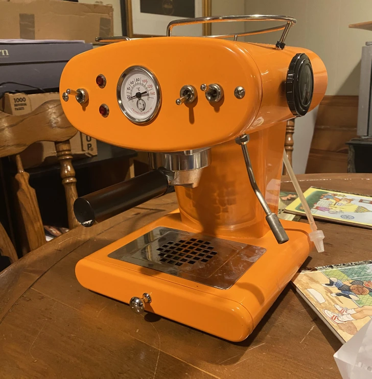 Oranžový retro kávovar s manometrom na drevenom stole, pripravený na prípravu lahodnej kávy.