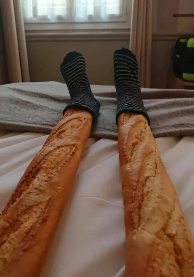 Dve bagety s ponožkami na posteli, vyzerajú ako nohy v pruhovaných ponožkách. Kreatívna optická ilúzia.