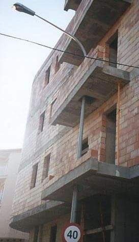 Nedokončená stavba z tehál so značkou obmedzenia rýchlosti na 40 km/h, zobrazená pod slabým denným svetlom.