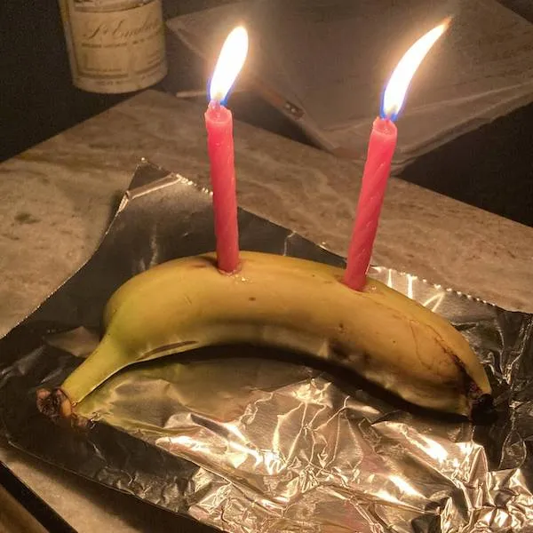 Banán s dvoma zapálenými sviečkami na alobale na stole, netradičný narodeninový dezert.