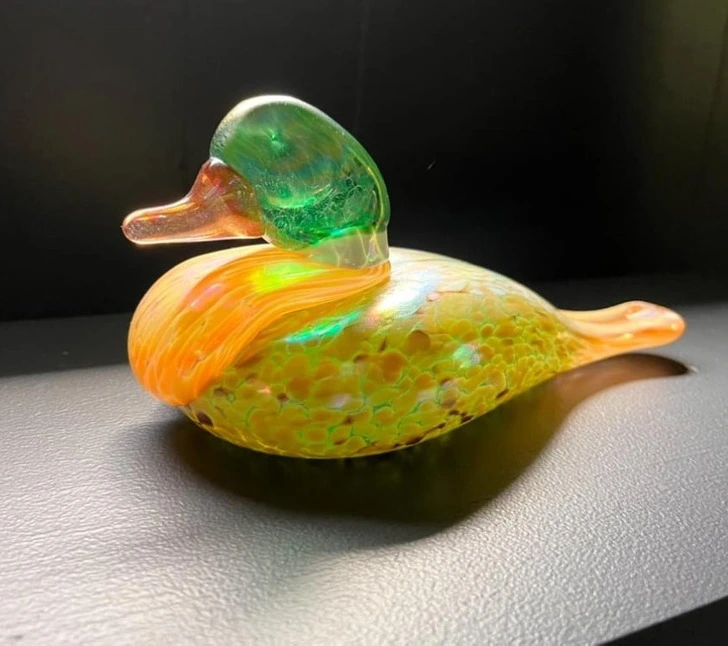 Sklenená kačka s dúhovými odleskami na čiernom povrchu. Ideálne pre dekoráciu moderného interiéru.