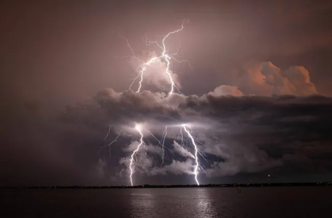Dramatická nočná búrka nad jazerom, zachytená viacerými bleskami osvetľujúcimi tmavé oblaky.