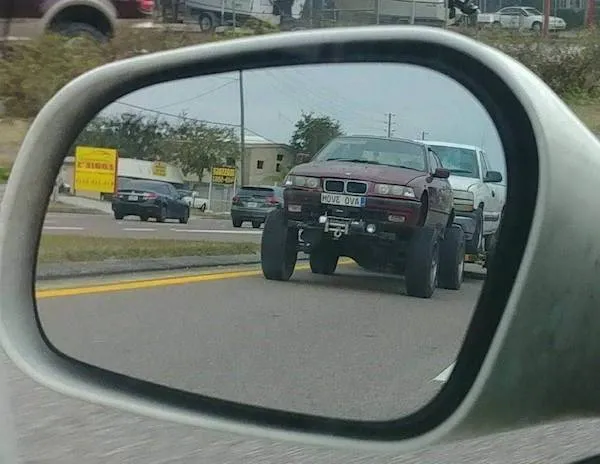 Auto s veľkými terénnymi kolesami v spätnom zrkadle na ceste.