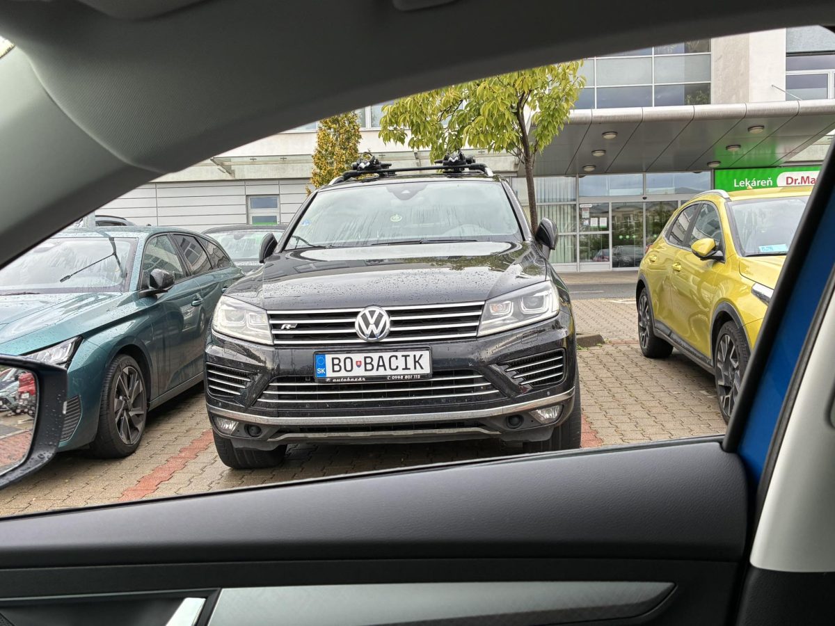 Čierny Volkswagen zaparkovaný medzi dvomi autami pred budovou s nápisom Lekáreň Dr. Max.