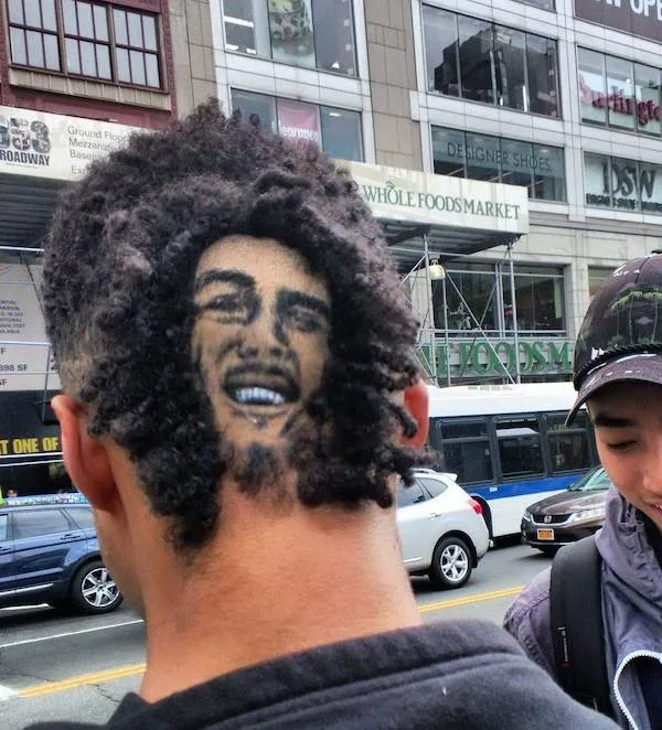 Osoba s originálnym účesom a obrazom tváre na zadnom časti hlavy na rušnej ulici v meste.