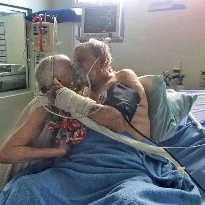 Starší pár sa objíma na nemocničnom lôžku, obaja s kyslíkovými maskami.