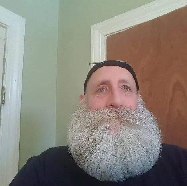 Muž s hustou bielou bradou a čiapkou stojí pred dverami.