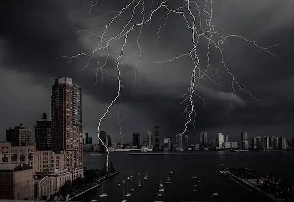 Búrka nad mestom s bleskami osvetľujúcimi tmavú oblohu nad mrakodrapmi a riekou.