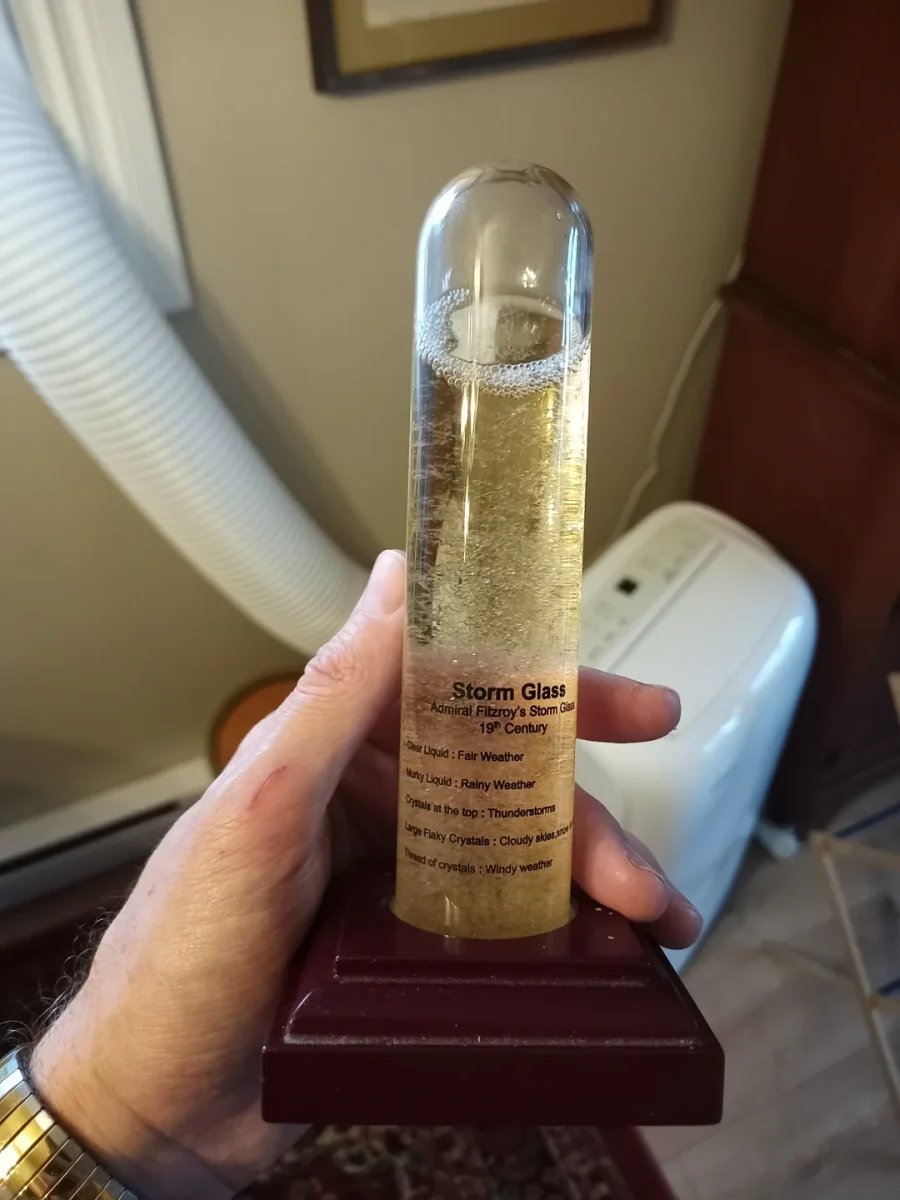 Historická búrková sklenená trubica na predpoveď počasia, držiak v ruke v interiéri.