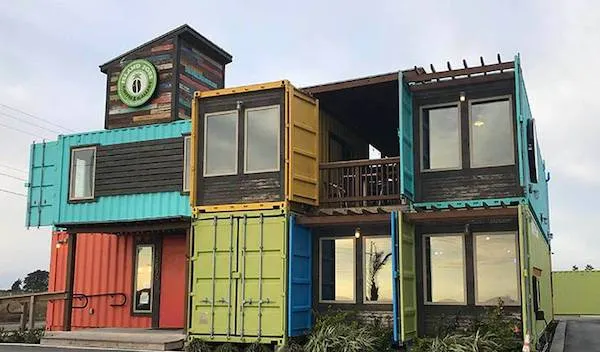 Moderná budova z recyklovaných prepravných kontajnerov so zelenými a modrými akcentmi.