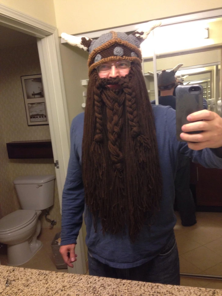 Osoba so sveterom a čiapkou s rohovinou pred zrkadlom, dlhá hnedá falošná brada, selfie v kúpeľni.