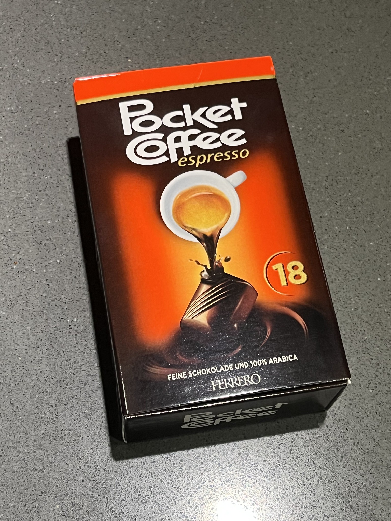 Krabička Pocket Coffee Espresso na šedej ploche, zloženie jemná čokoláda a 100% arabica, 18 kusov.