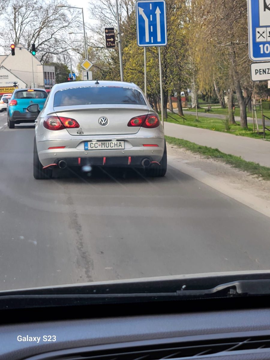 Auto značky Volkswagen na ceste so zaujímavou poznávacou značkou a dopravnými značkami v pozadí.