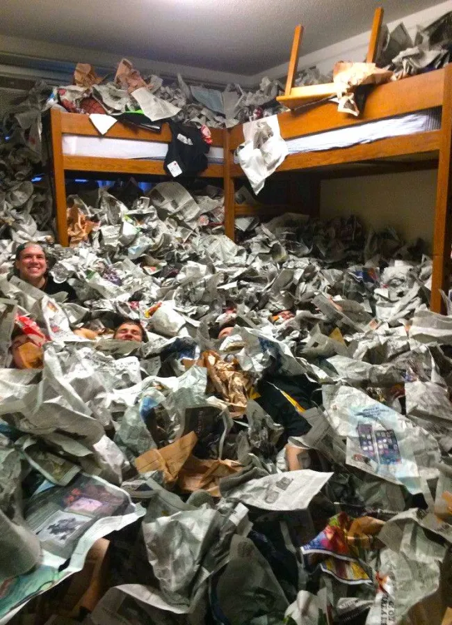 Izba s poschodovými posteľami zavalená množstvom novín, len hlavy dvoch osôb sú viditeľné nad papierom.