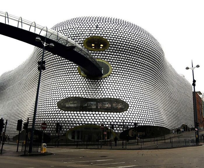 Futuristická budova pokrytá kovovými diskami s premostením v mestskom prostredí.