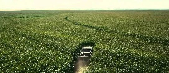 Auto jazdí cez zelené pole, vytvára za sebou stopu v nekonečných lánoch úrody pod jasnou oblohou.