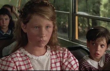 Deti sediace v autobuse s vážnymi výrazmi na tvárach, letný deň a zelená krajina vonku.