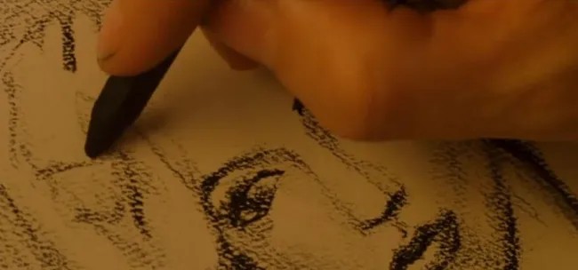 Ruka kresliaca ceruzkou portrét na papieri, zachytávajúca detaily tváre umelca v procese tvorby.