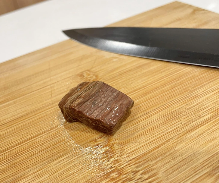 Kocka mäsa na drevenej doske s nožom v pozadí, pripravená na krájanie v kuchyni.