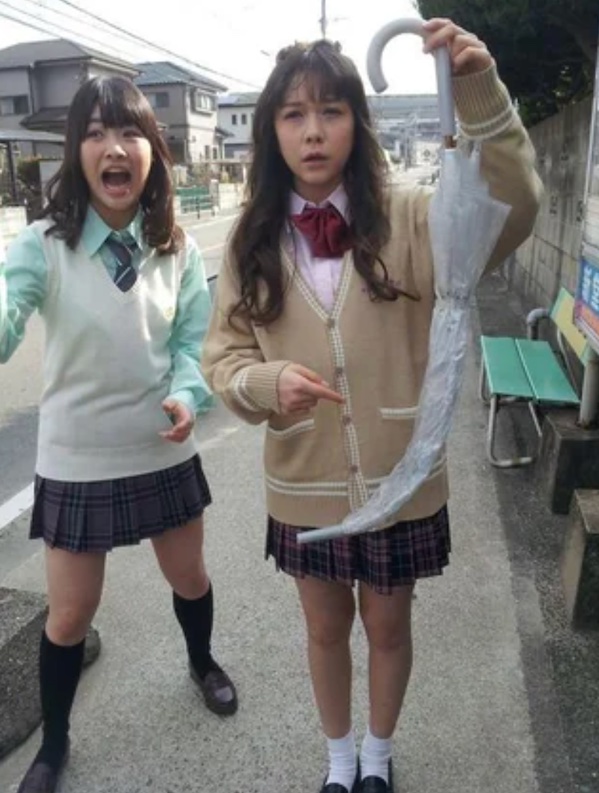 Dve dievčatá vo uniformách ukazujú na neobvykle zdeformovaný dáždnik na ulici.