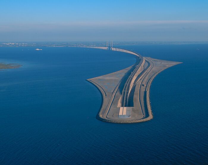 Letecký pohľad na most cez more s ostrovom spájajúcim dve krajiny, modrá obloha a pokojná hladina vody.