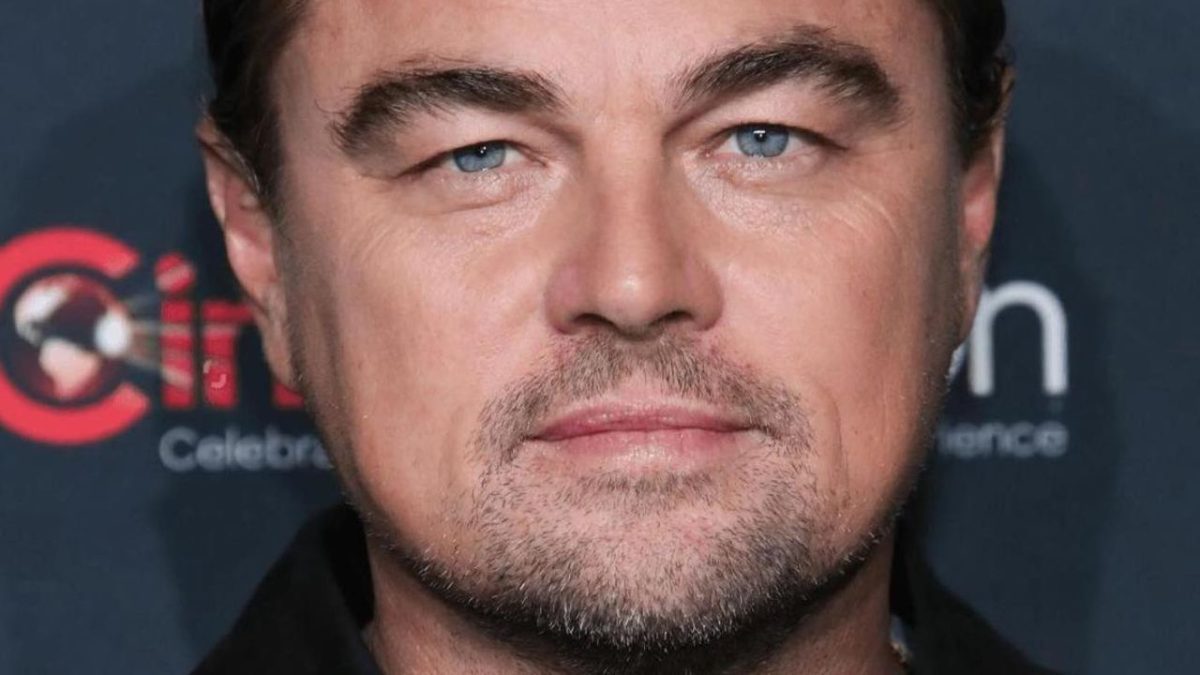 Osoba s modrými očami a svetlou bradou na podujatí. Pozadie s rozmazaným logom.