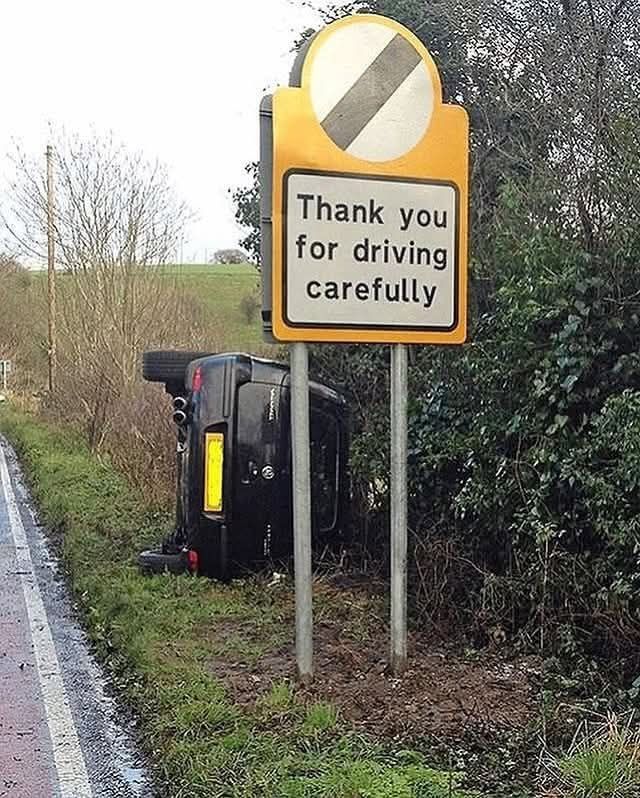 Auto prevrátené na boku vedľa cesty, vedľa dopravnej značky s textom Thank you for driving carefully.