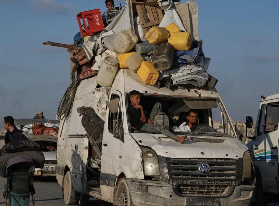 Dodávka naložená vecami, ľudia sedia na kapote, modrá obloha, pohyb na neistých cestách.