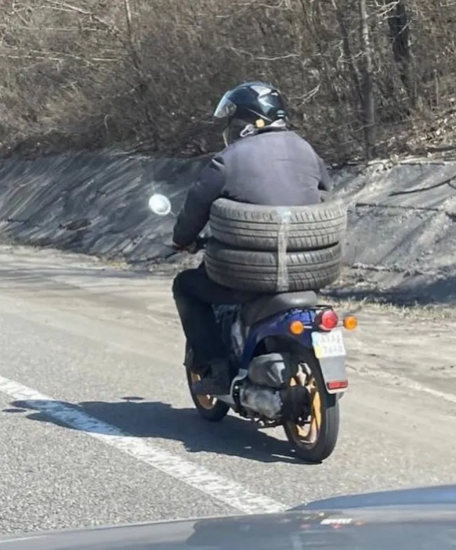 Motorkár nesie štyri pneumatiky na chrbte, jazda na vidieckej ceste, bezpečnostná výzva.