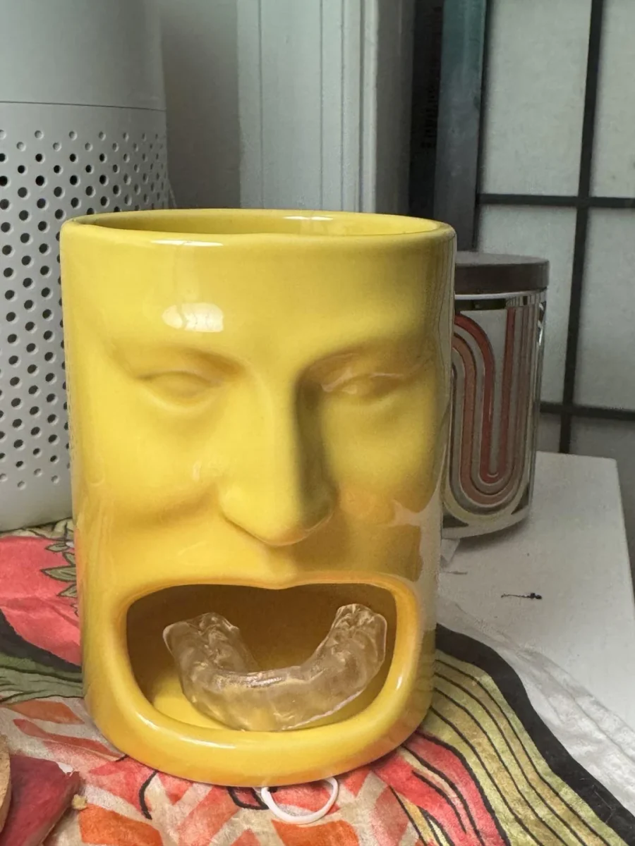 Žltý keramický držiak na chránič zubov s tvárou na farebnom obruse.