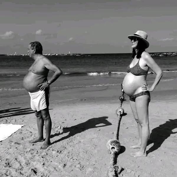 Dve osoby s veľkými bruškami sa opaľujú na pláži, vizuálne pripomínajú boj s kotvou na piesku.