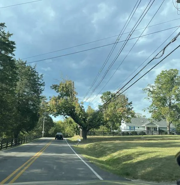 Vidiek s cestou, dreveným plotom, domom a mrakmi na oblohe.