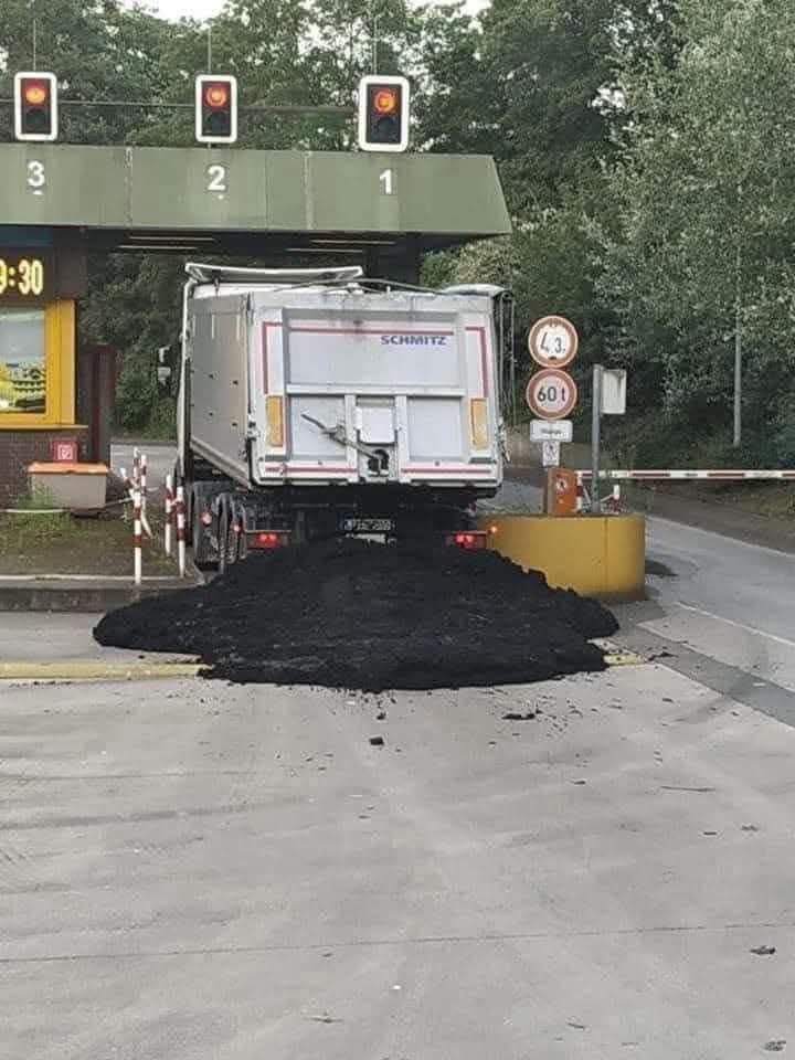 Nákladné auto prechádzajúce mýtnou bránou so zosypaným nákladom uhlia na ceste.