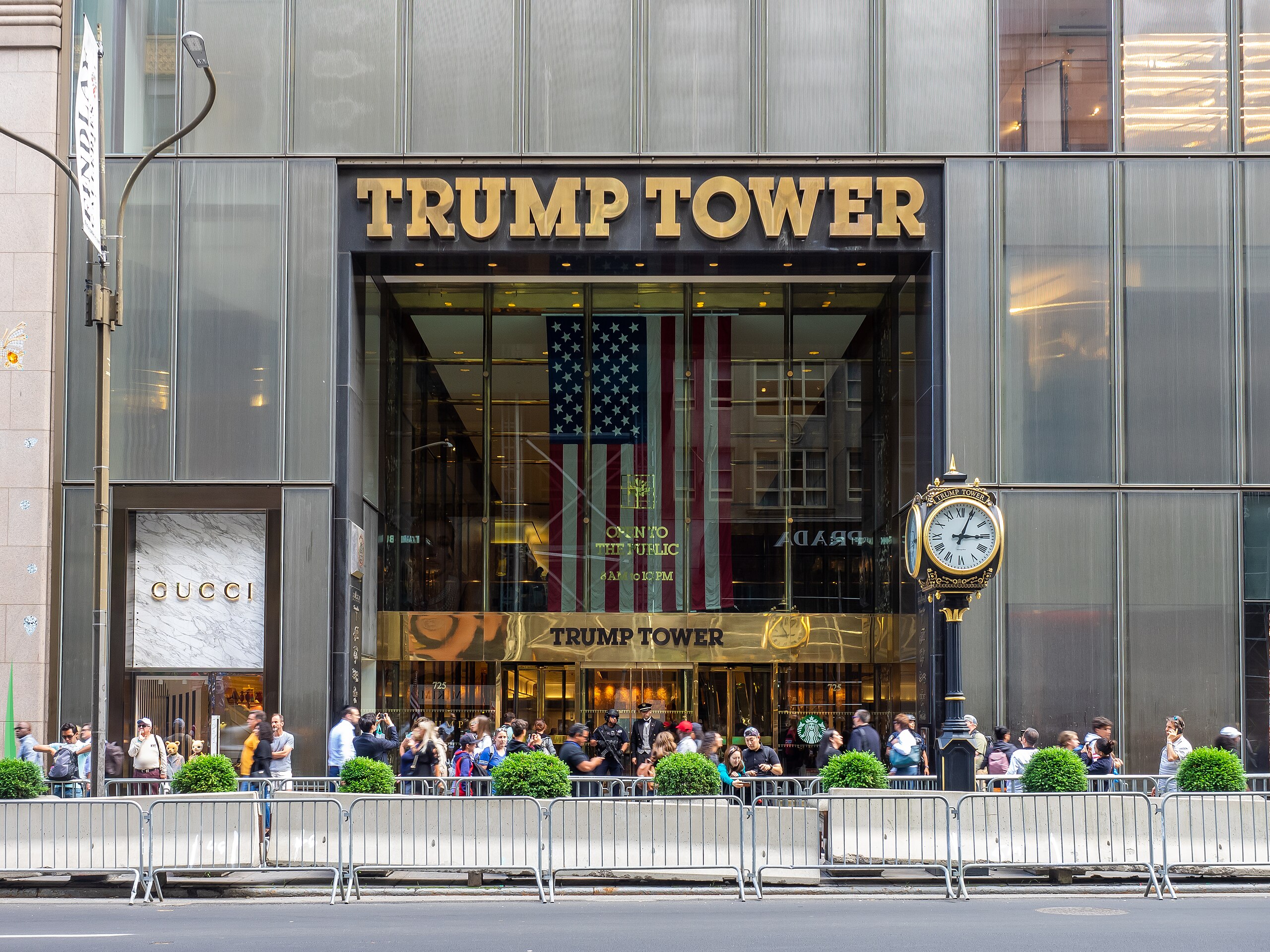 Budova Trump Tower s davmi ľudí pred hlavným vchodom, zlaté logo a historické hodiny v popredí.