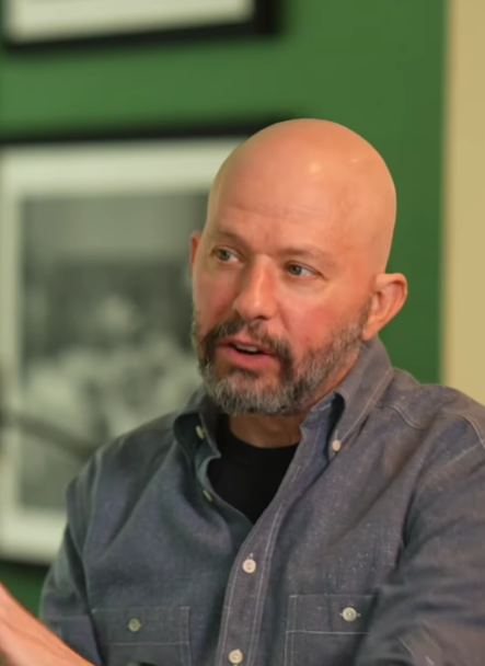 Bezpopisová osoba v debate, zelené pozadie, čiernobiela fotografia na stene.